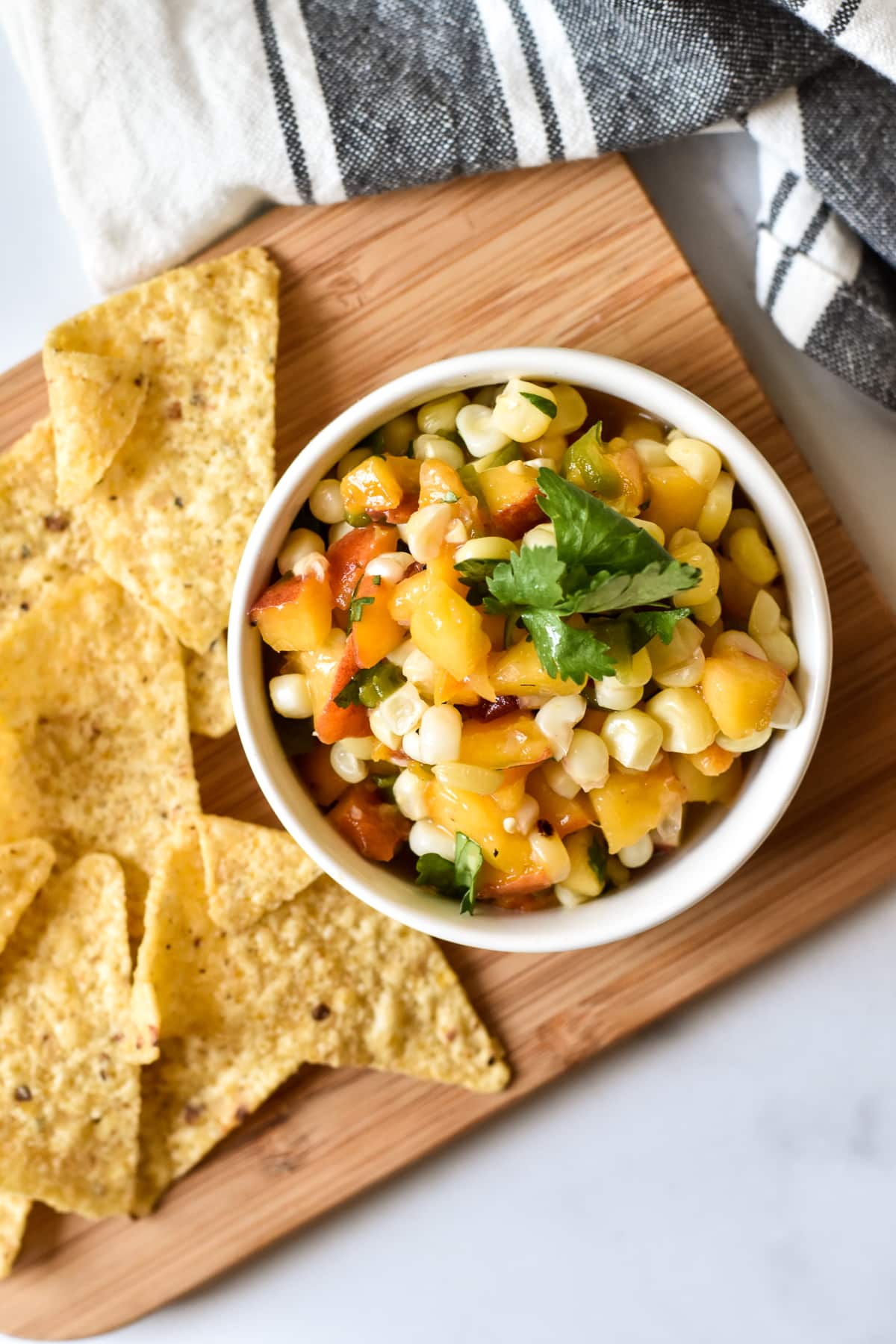 dish of peach, corn and chile salsa with chips on a wood cutting board