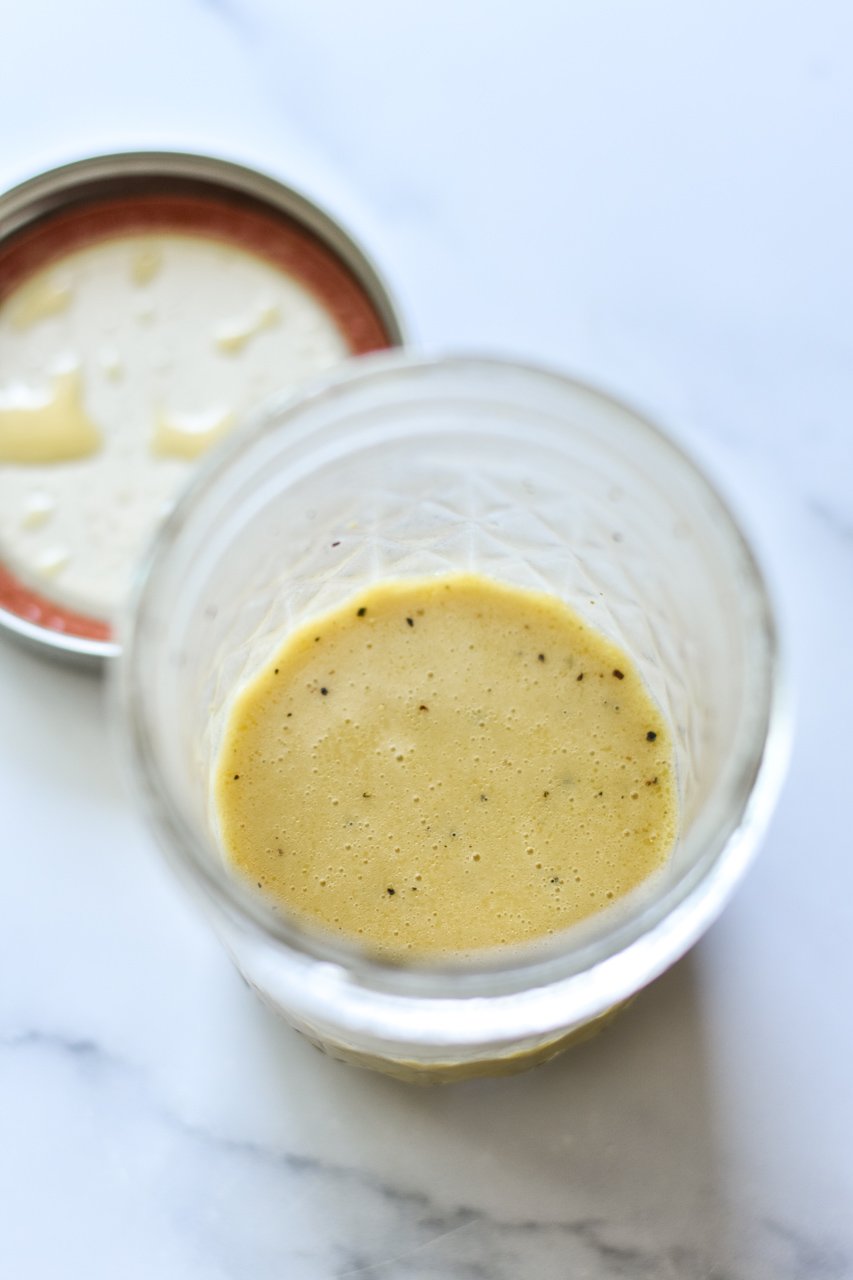 lemon dijon dressing in a small mason jar with lid off to the side