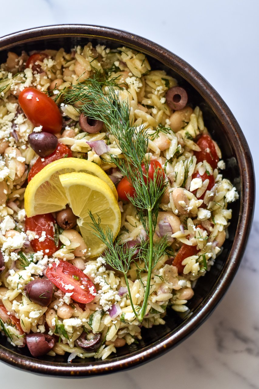 greek orzo salad in a serving bowl with lemon and dill on top