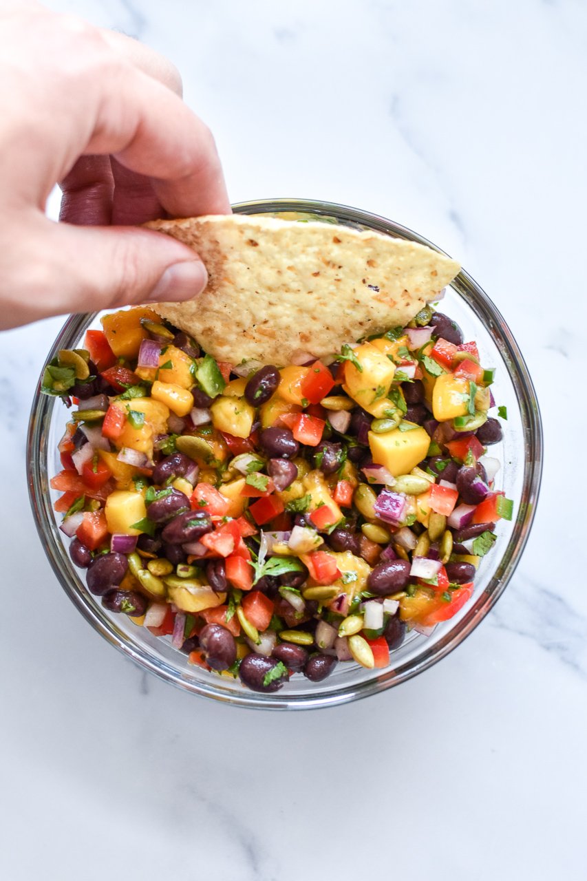 dipping a tortilla chip in mango black bean salsa