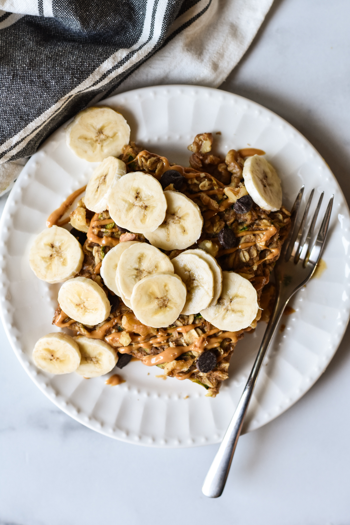 square of baked oatmeal on a plate topped with peanut butter and sliced bananas