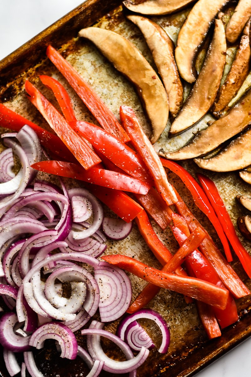 sliced mushrooms, red bell peppers and onions on a sheet pan