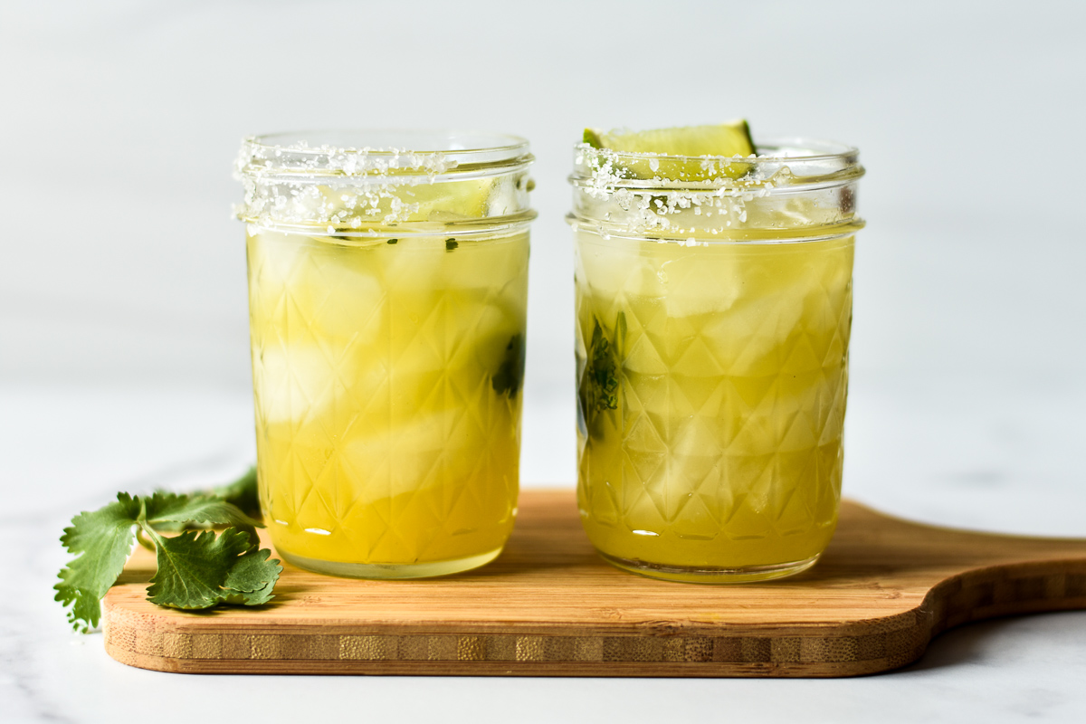 two margaritas on a wooden cutting board with cilantro garnish