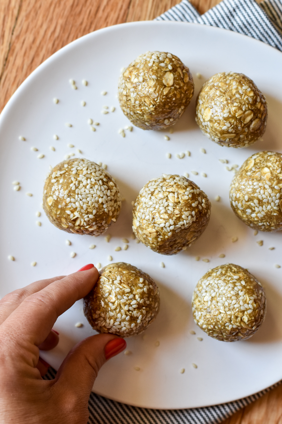 maple tahini oatmeal balls rolled in sesame seeds on a plate with fingers picking one up