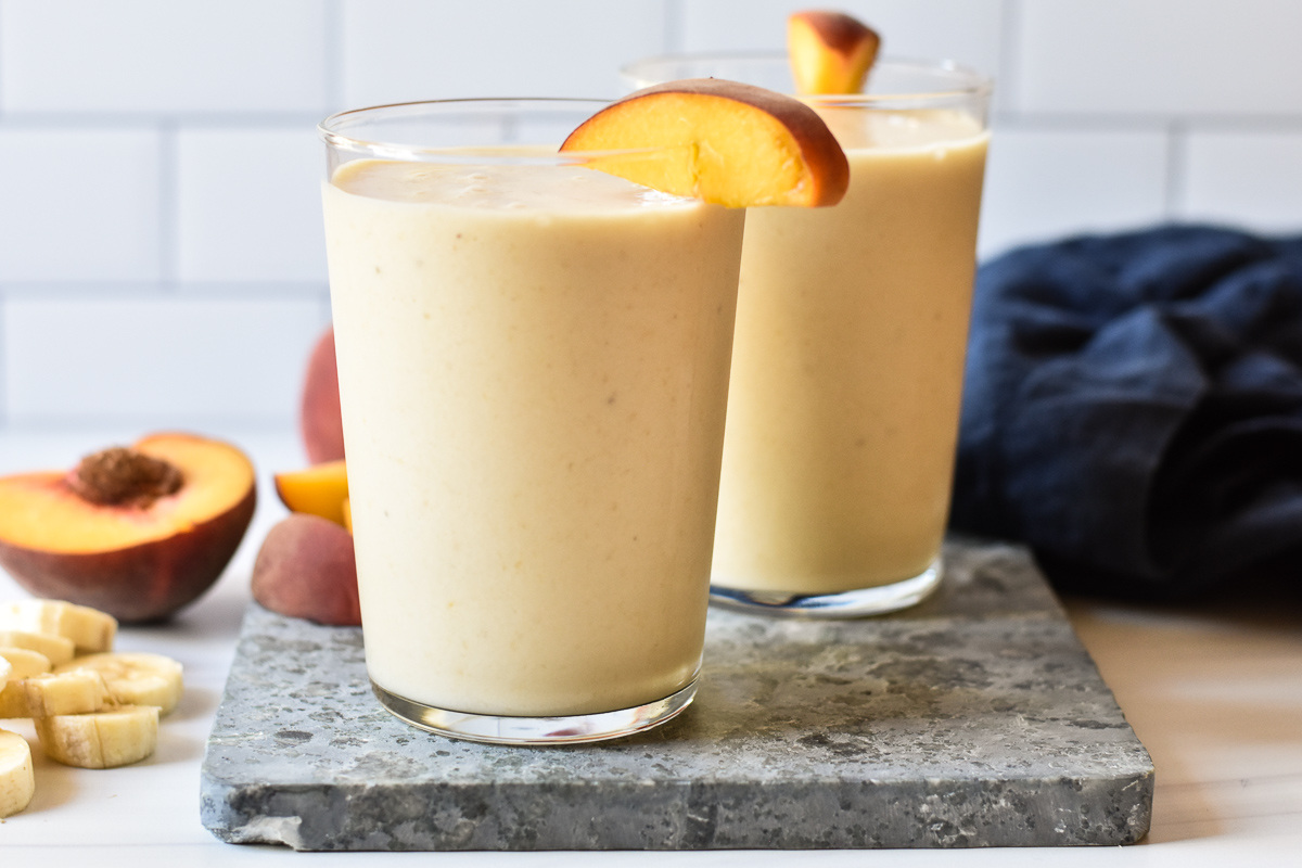 two glasses of smoothie with peach on rim