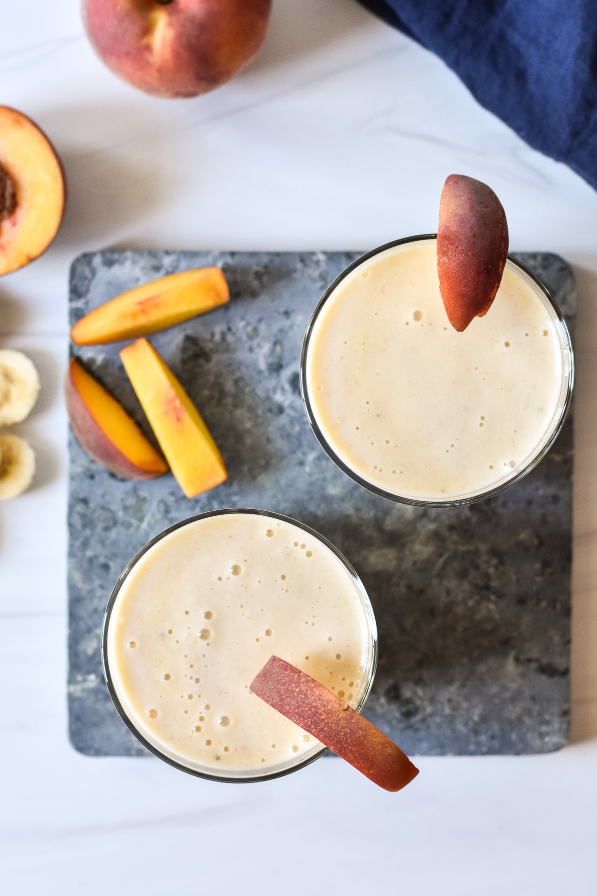 two smoothies with peach slices on rim