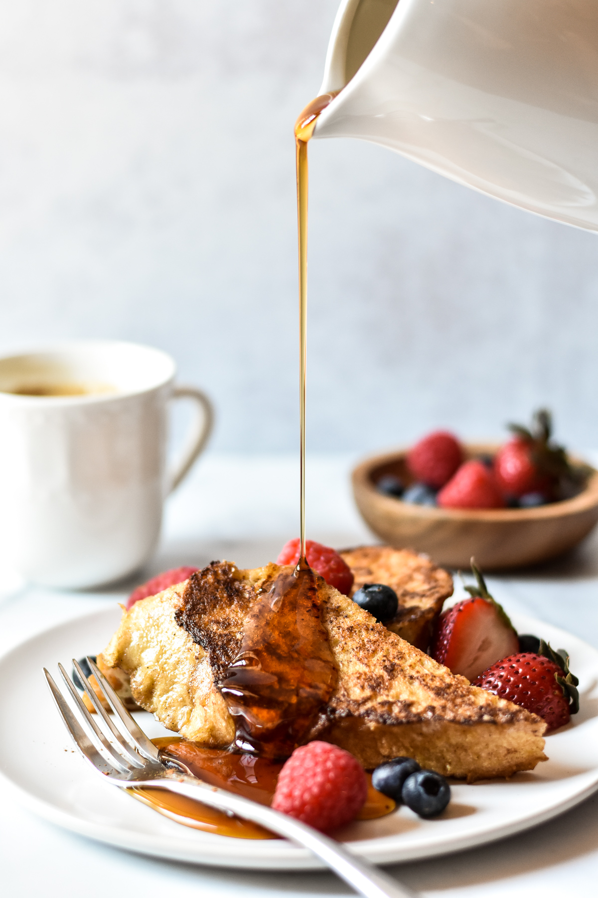 sourdough french toast with stream of syrup and berries in the background