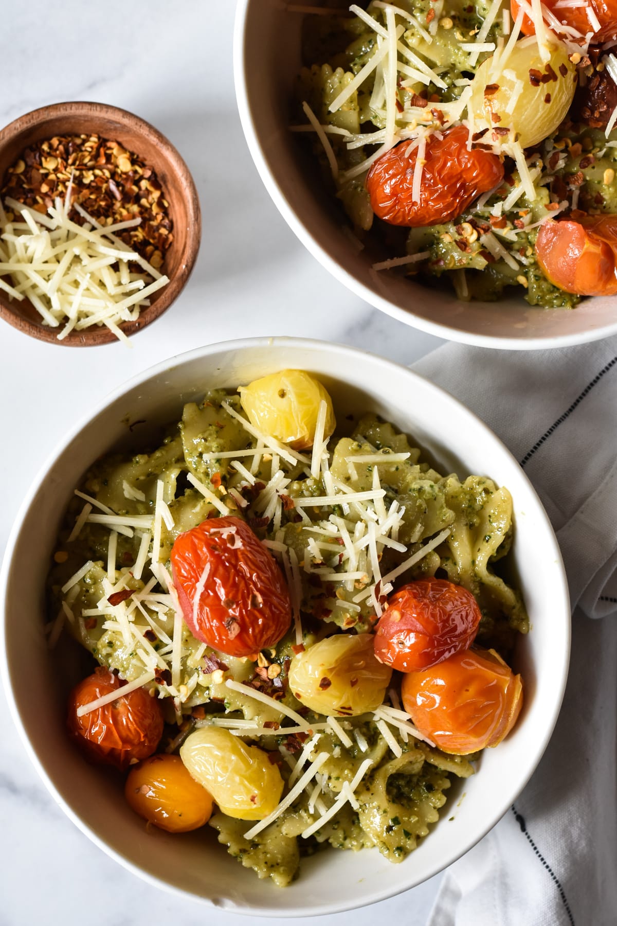 bowl of pesto pasta topped with tomatoes and parmesan cheese