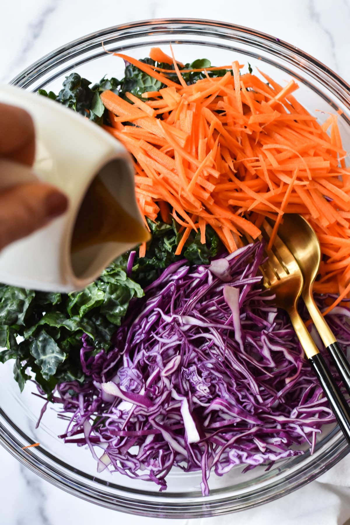 purple cabbage, carrots and kale in a bowl with dressing pour