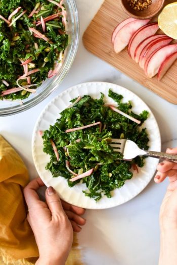 plate of kale crunch salad with hand on fork
