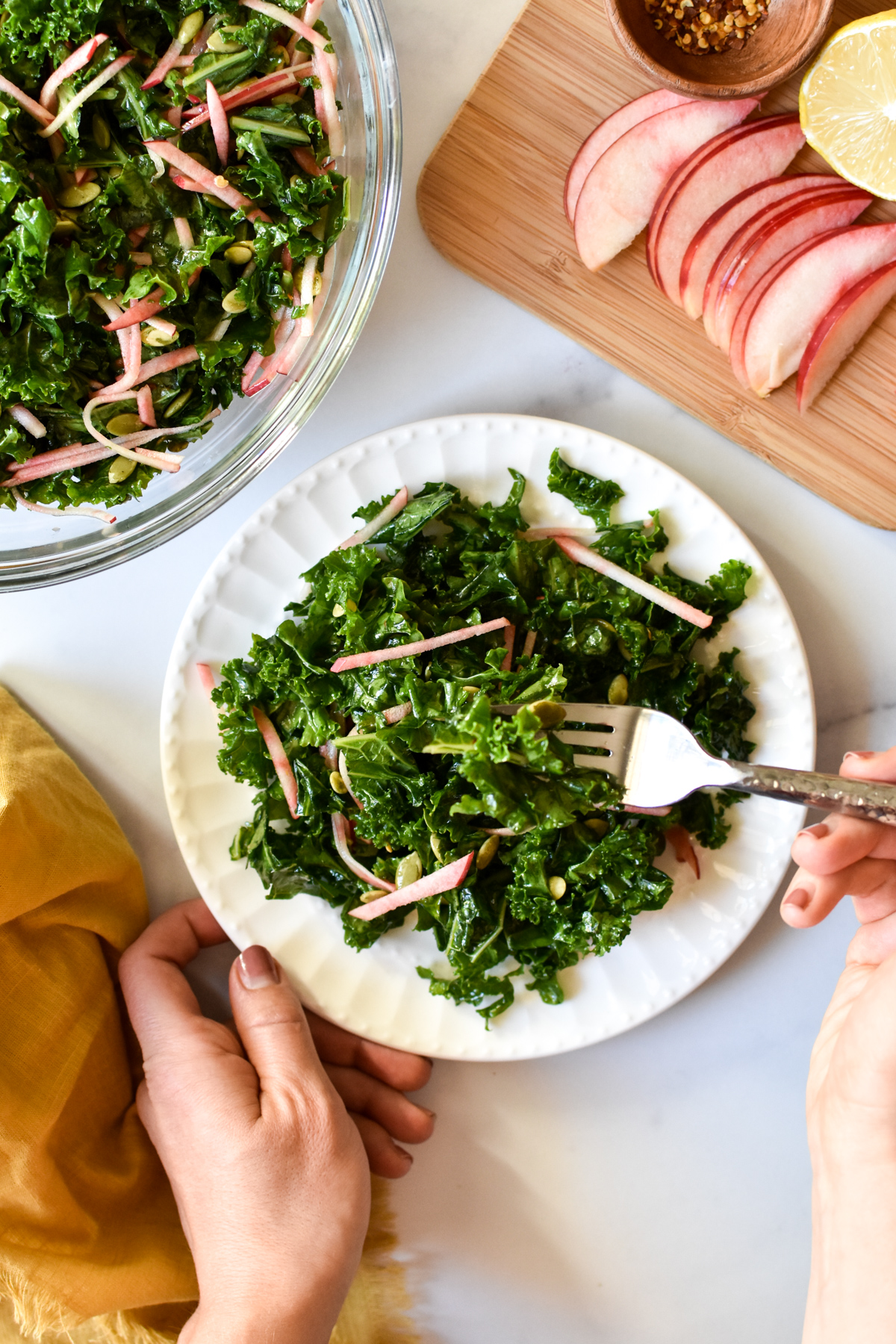 plate of kale crunch salad with hand on fork and apples in background