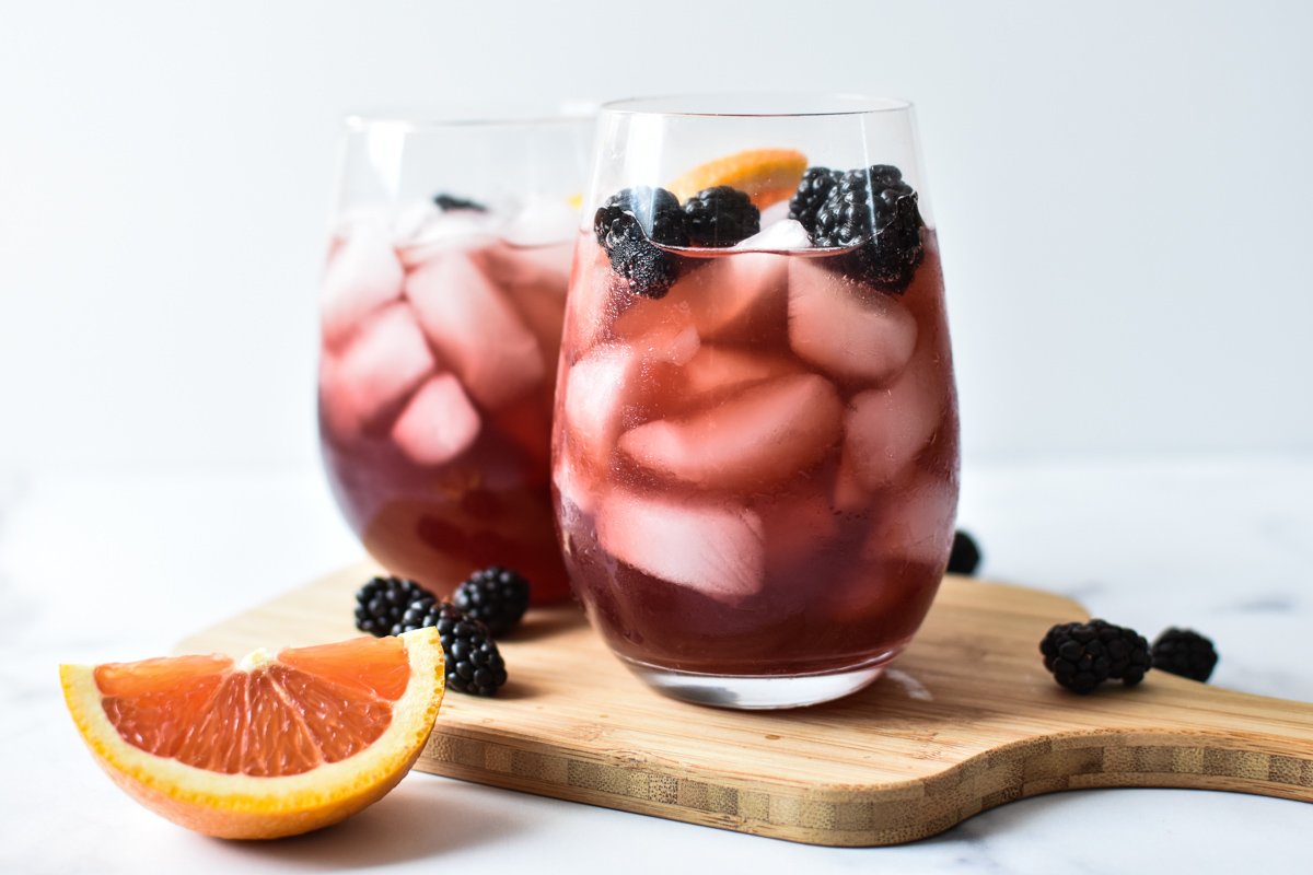 two sangria mocktails on wooden cutting board with an orange wedge