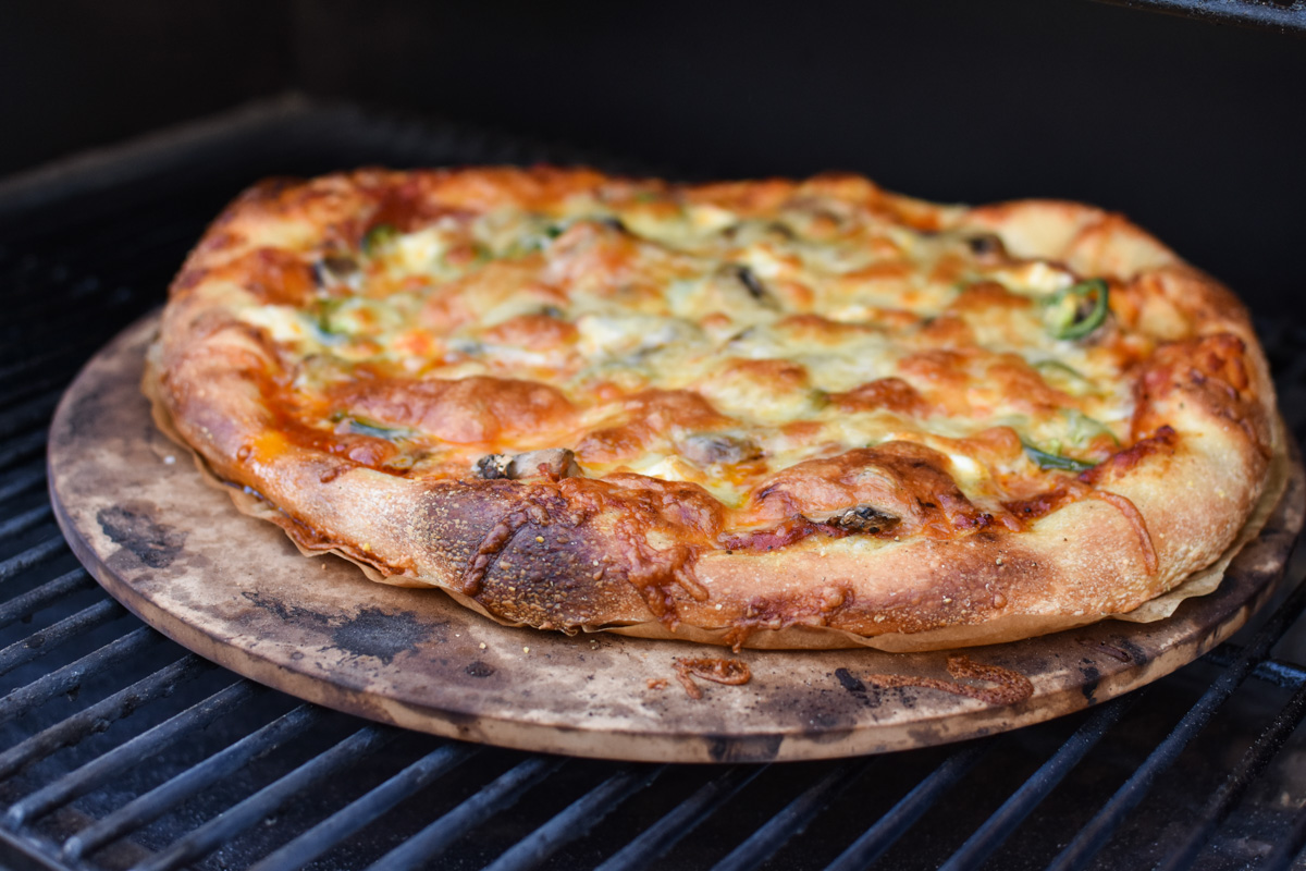 cooked pizza on a pizza stone on the grill