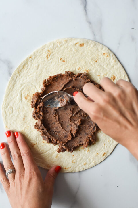 spreading refried beans on a tortilla