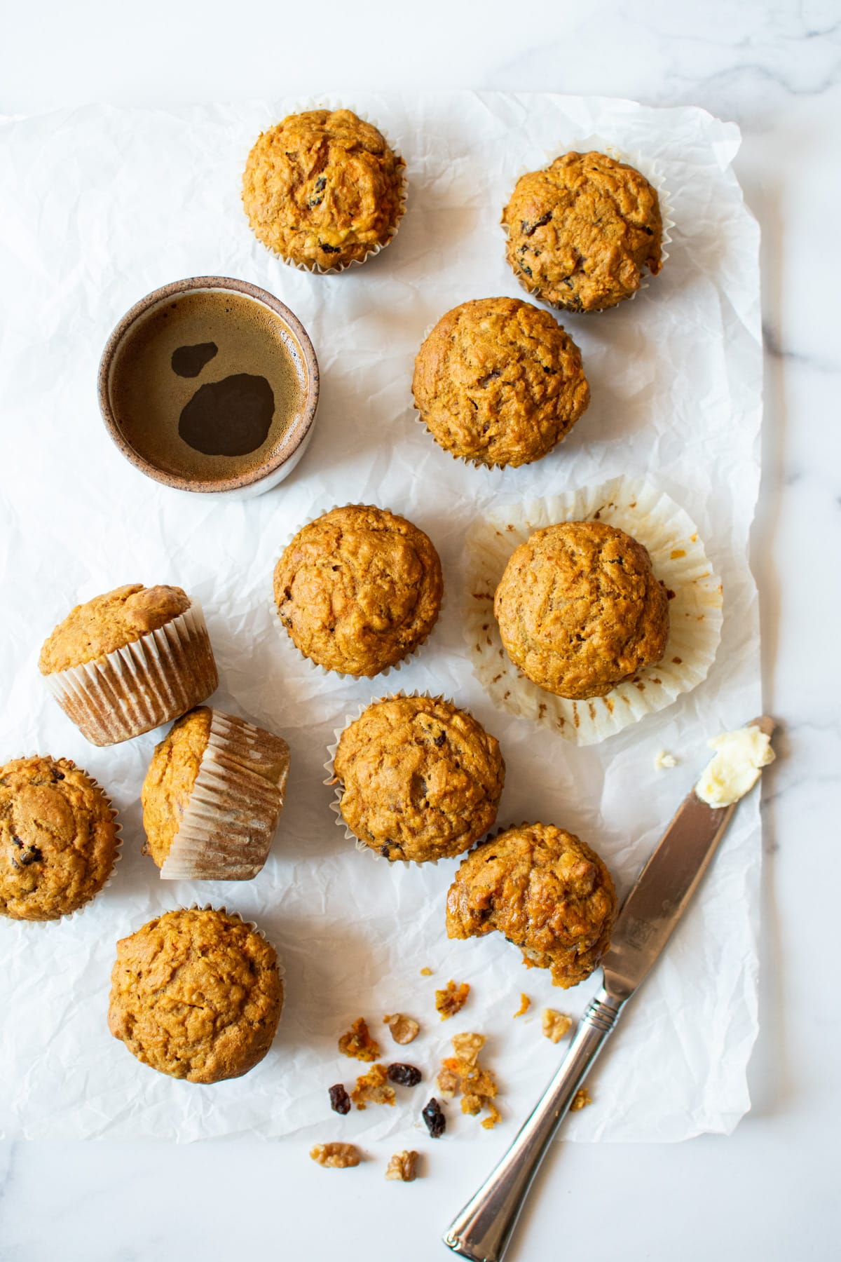 banana carrot muffins scattered on parchment paper with butter knife and cup of coffee
