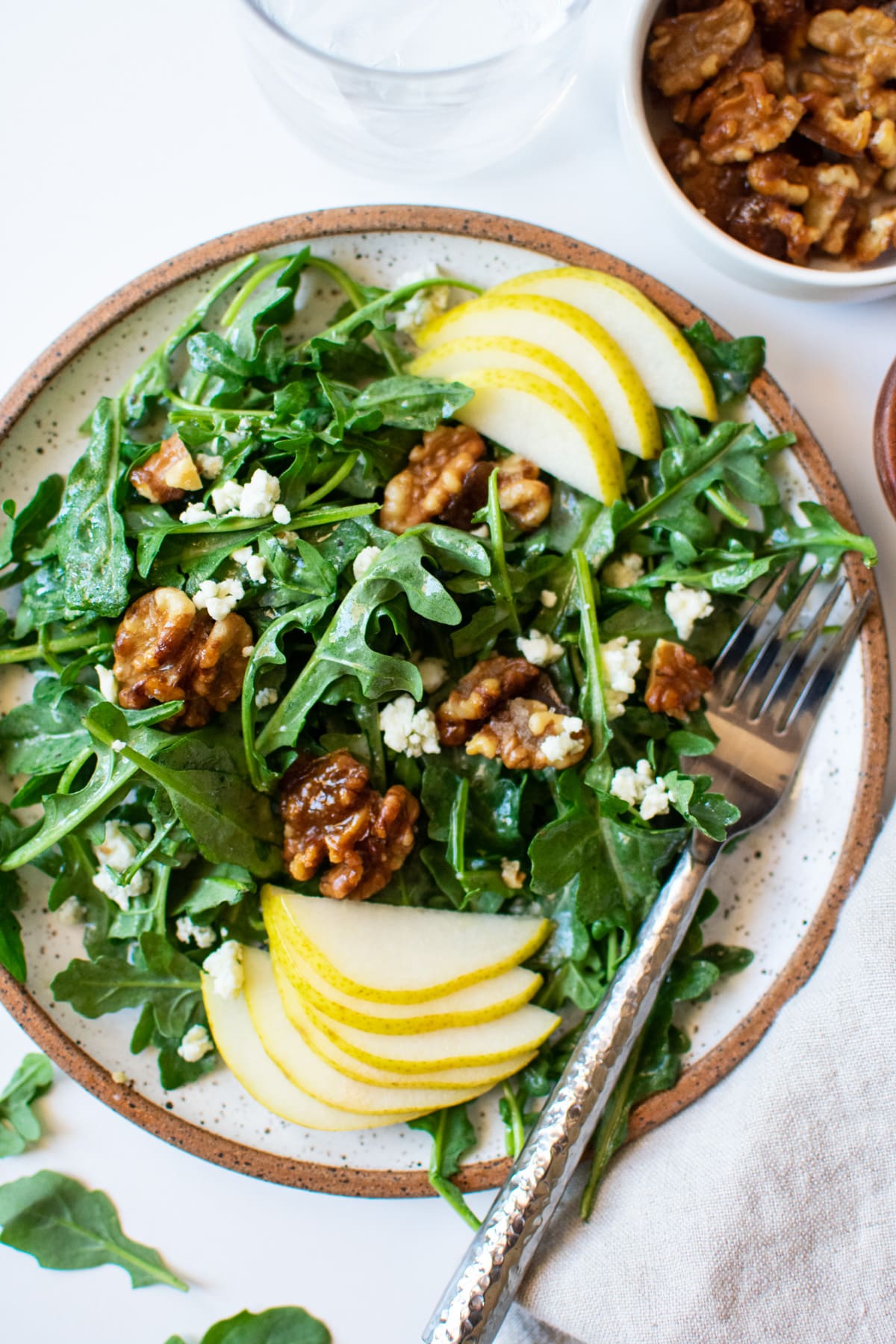 arugula pear salad on a plate with extra candied walnuts on the side