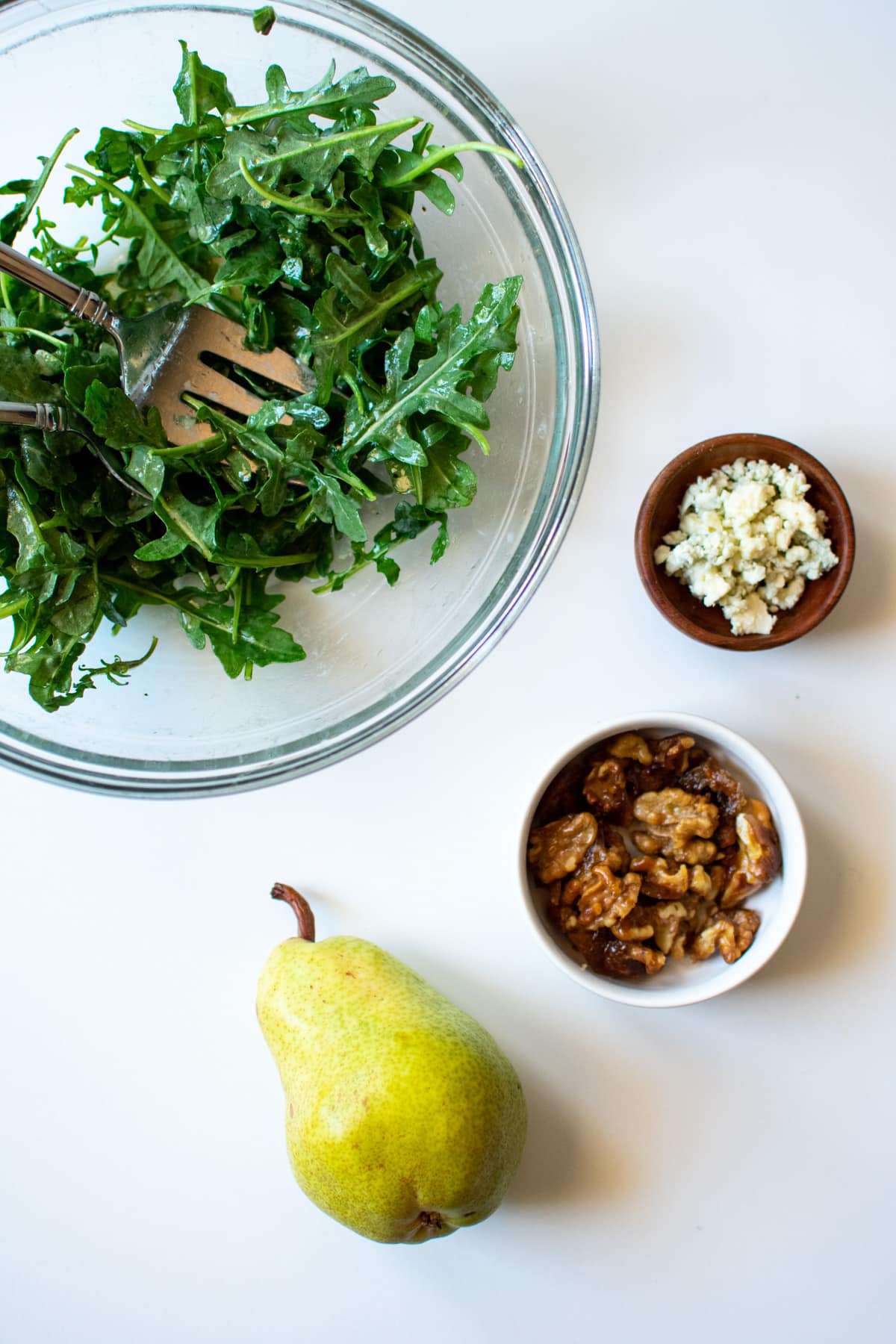 arugula in a bowl, bleu cheese crumbles, walnuts and a pear