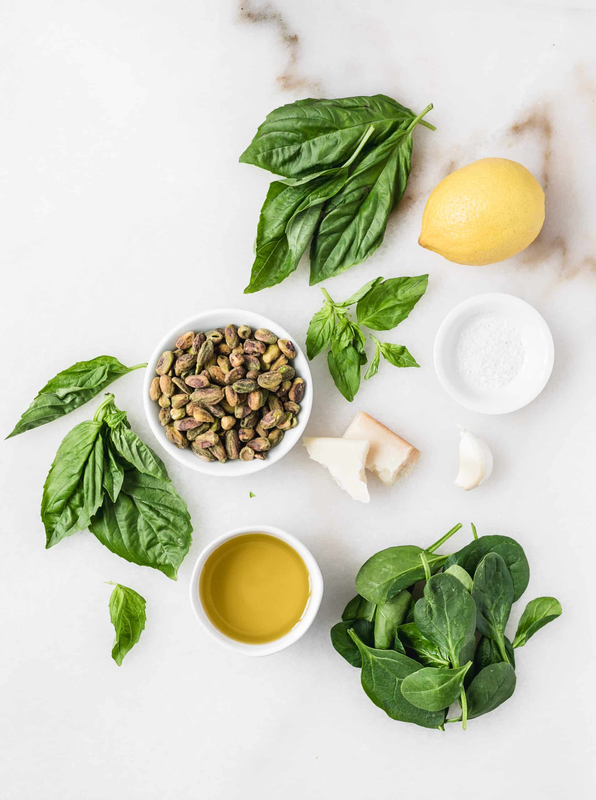 basil, lemon, salt, parmesan cheese, garlic clove, pistachios in a bowl, olive oil and spinach leaves