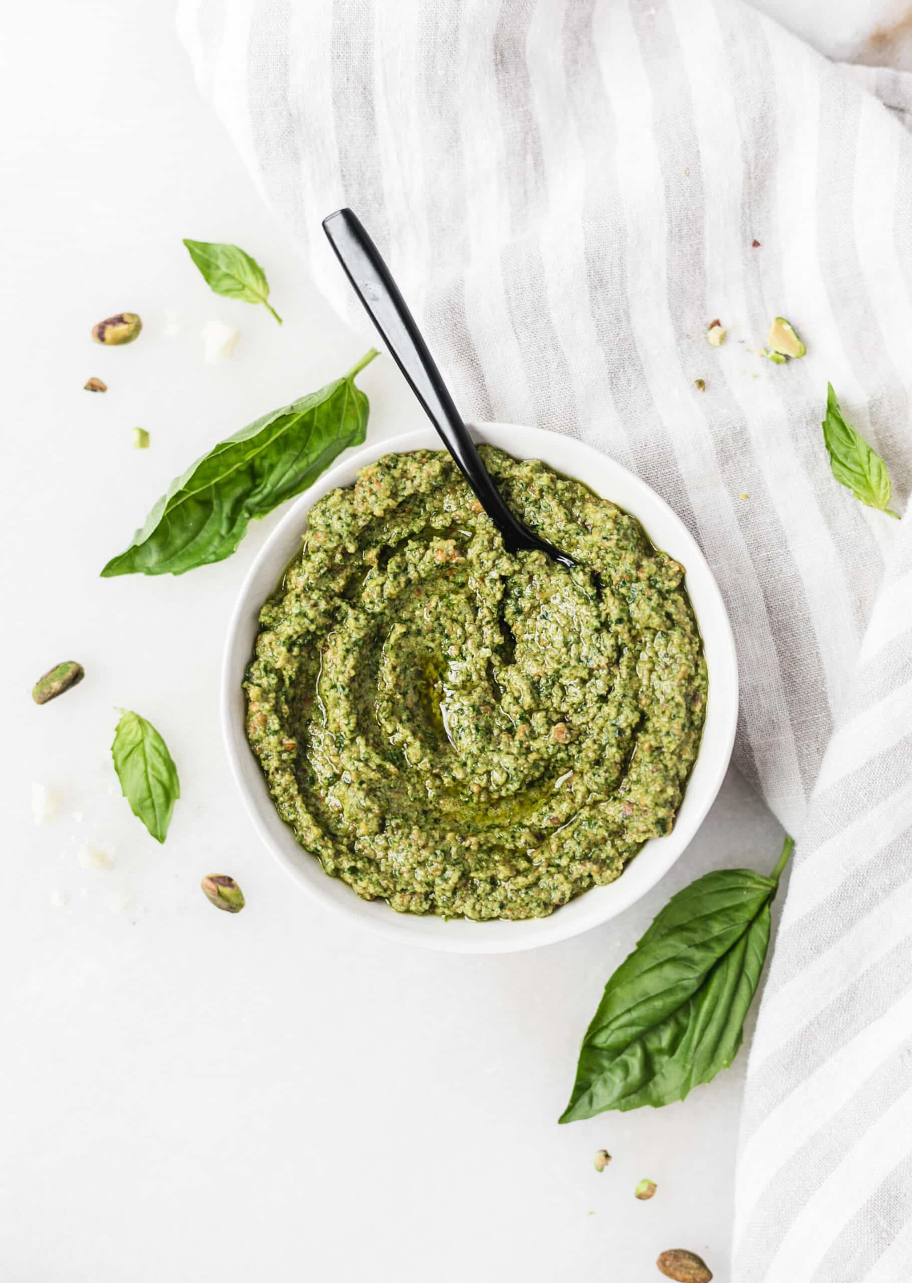 pistachio pesto in a bowl with a spoon and basil leaves scattered