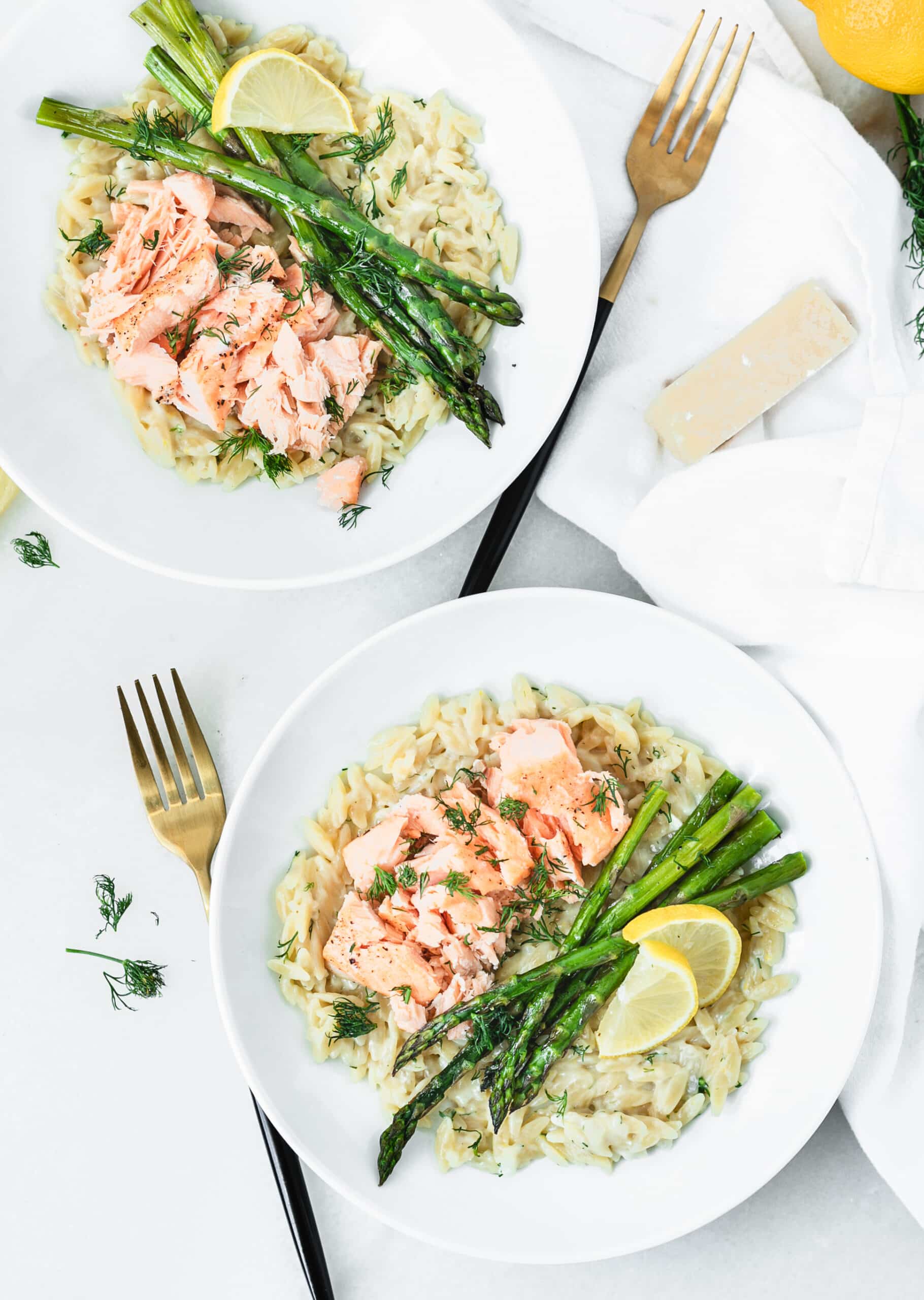 plates of creamy lemon parmesan orzo with salmon and asparagus with forks on the side 