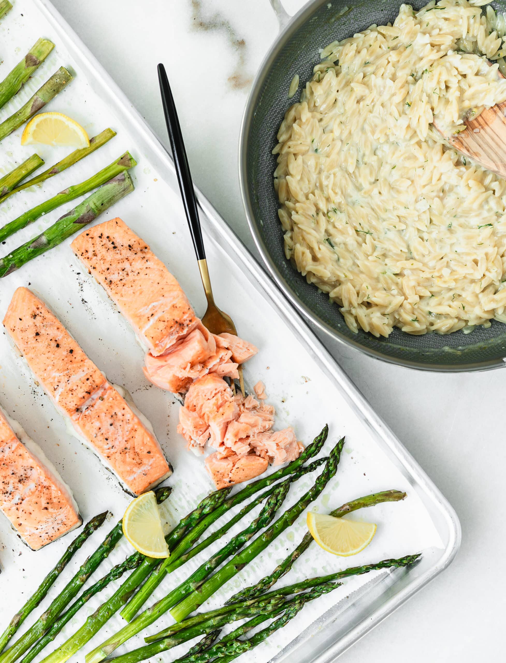 creamy orzo in a skillet with salmon and asparagus on a sheet pan