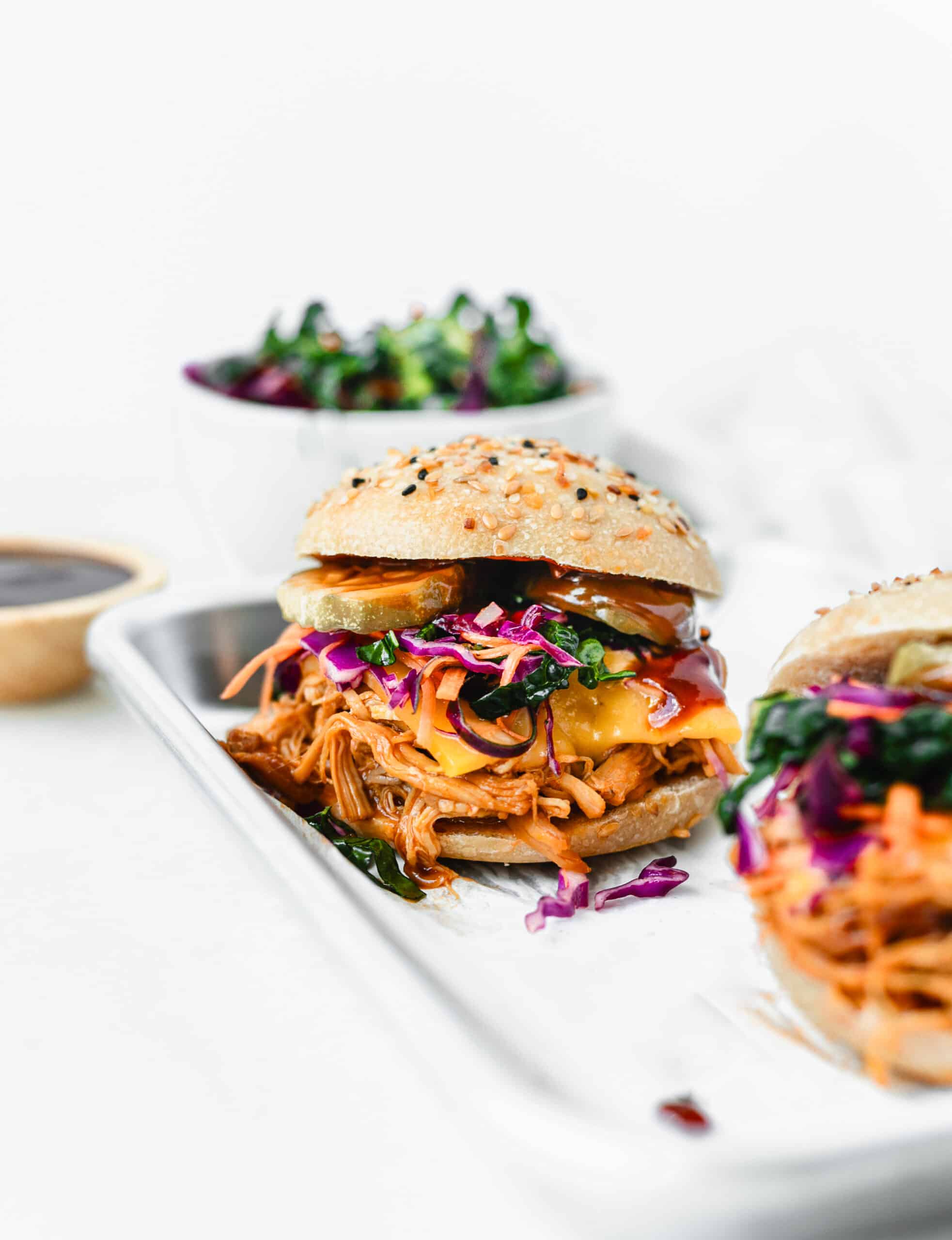 bbq chicken sandwich with cheese, slaw and pickles on a seedy bun