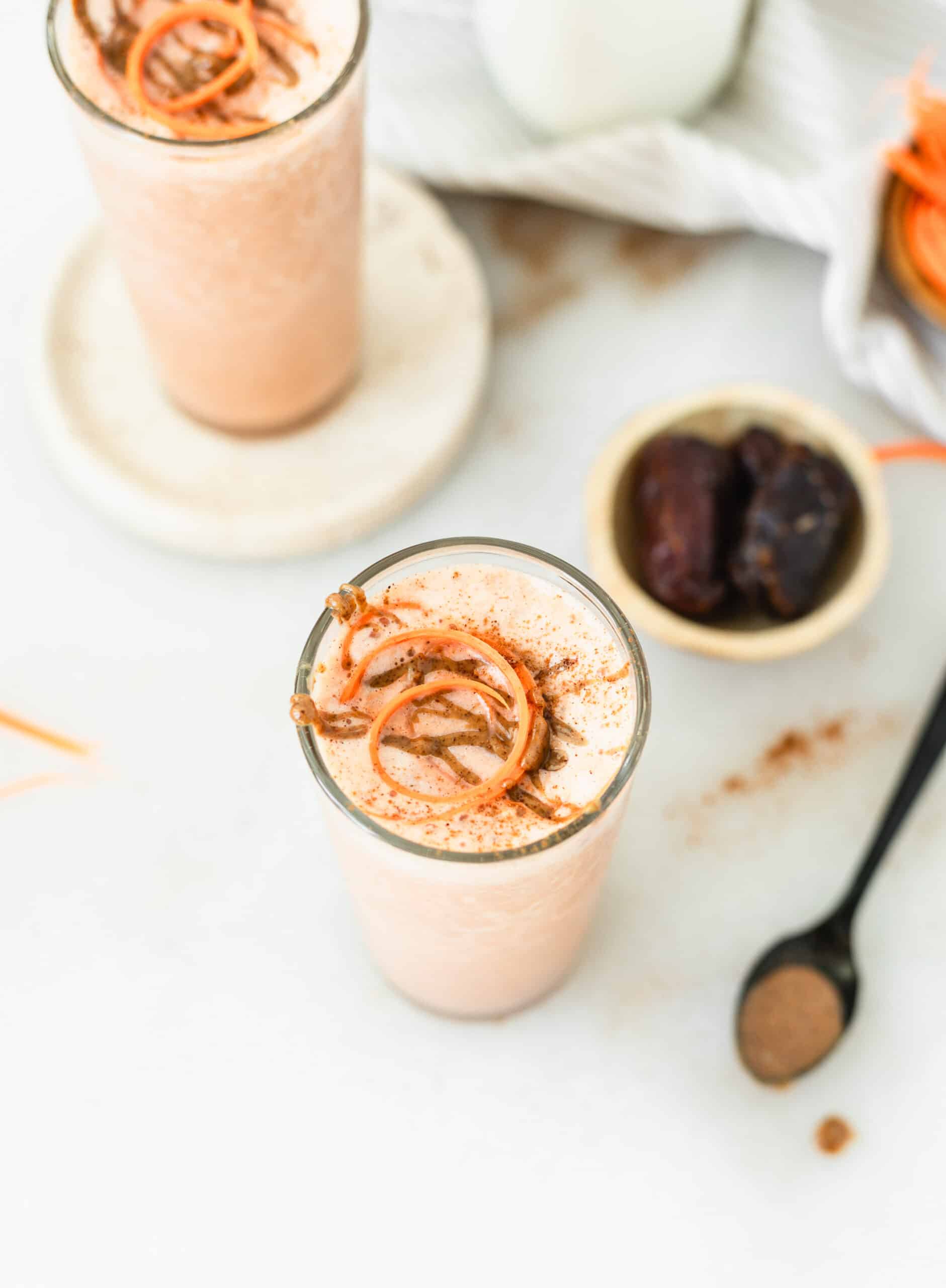 carrot banana smoothie in a glass with almond butter drizzle and carrot shred on top