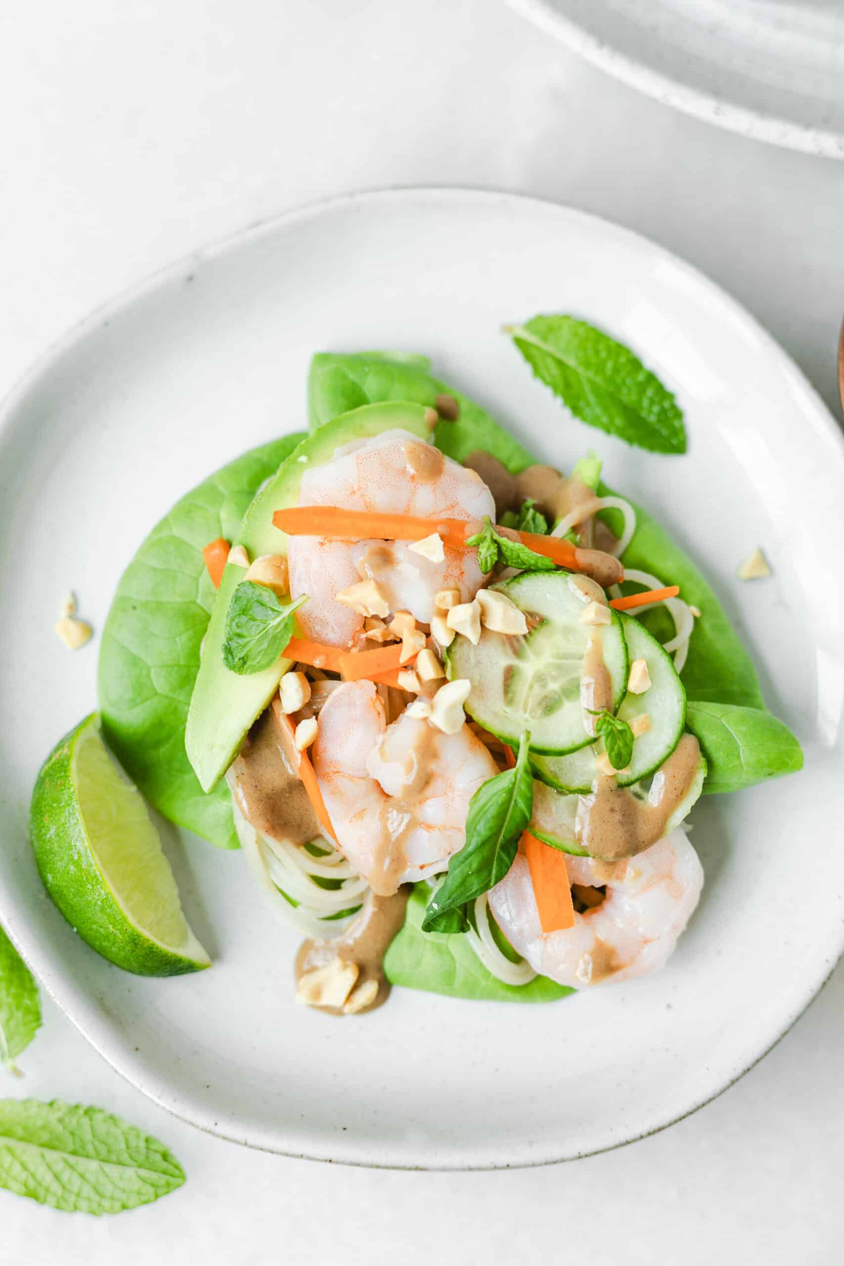 overhead closeup of a lettuce leaf with shrimp, cucumbers, peanuts and avocado
