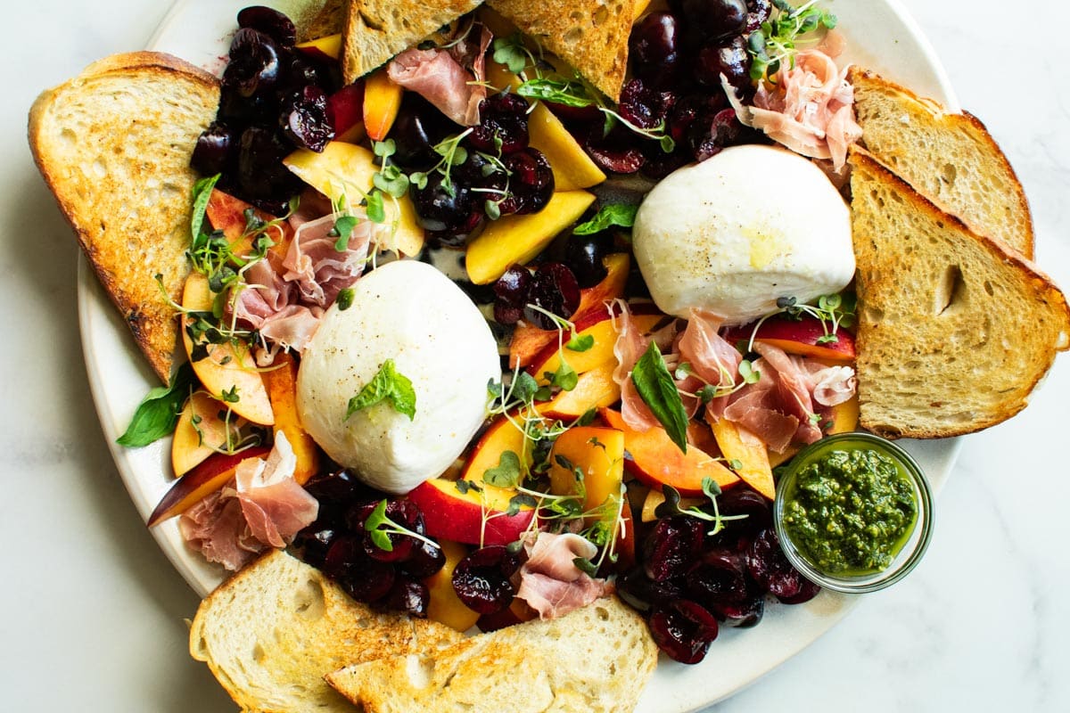 a platter of fruit, grilled bread, pesto, burrata cheese and greens