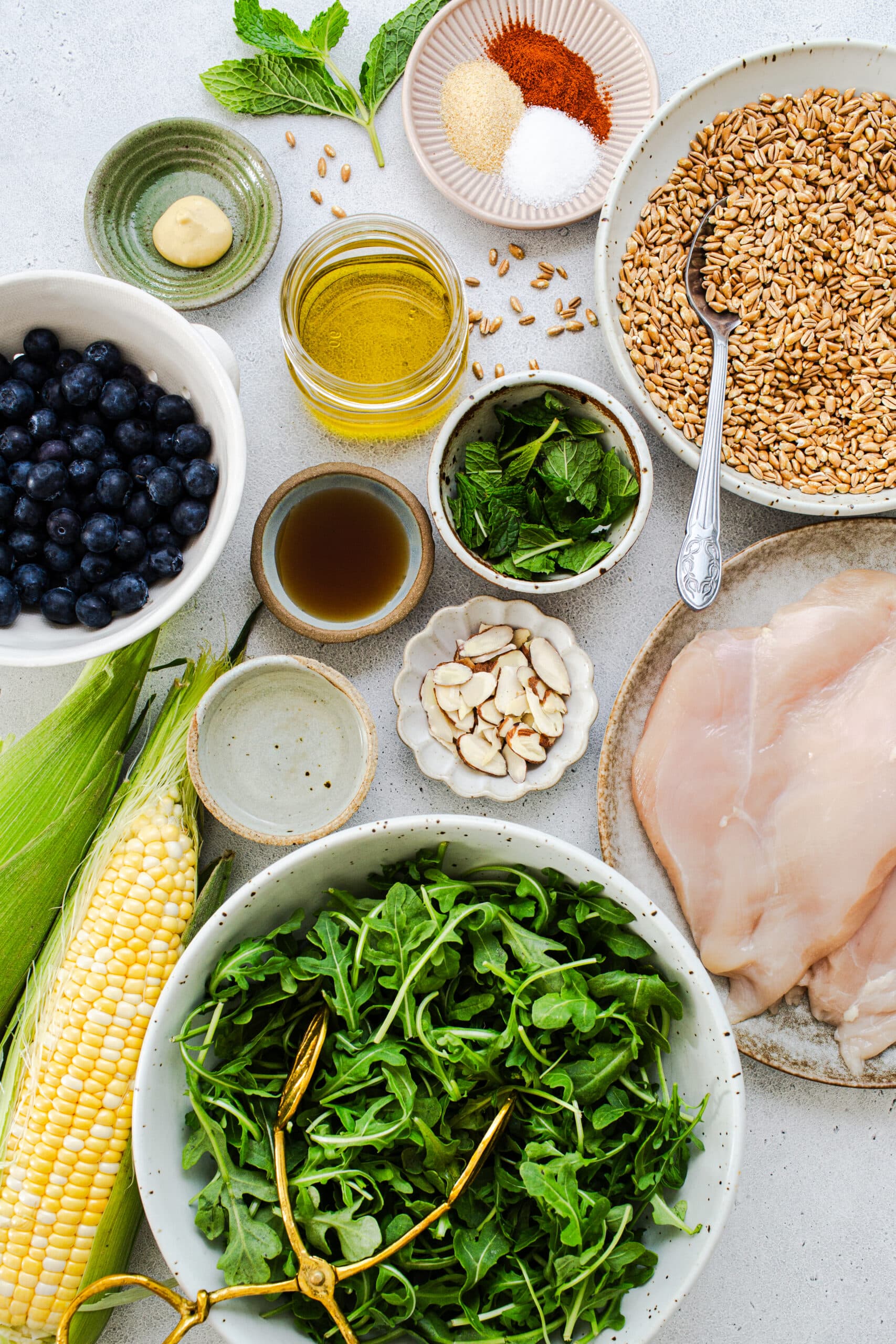 ingredients for healthy summer farro including blueberries, farro, arugula corn and almonds in separate dishes